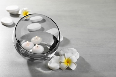 Vase of water with burning candles and spa stones on grey table, space for text