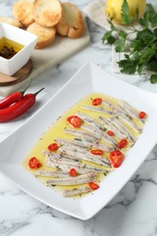 Tasty pickled anchovies with spices and products on white marble table