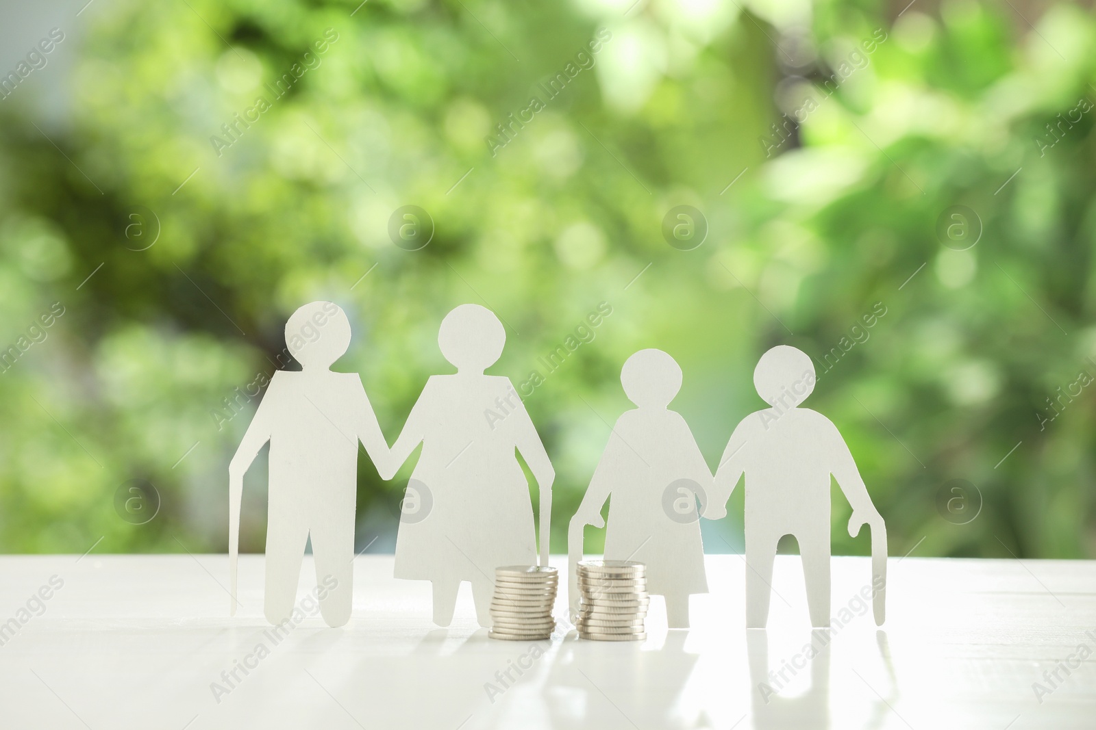 Photo of Pension savings. Figures of elderly people and coins on white table against blurred green background