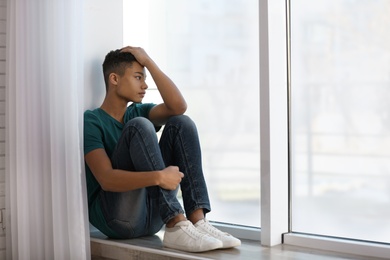 Upset African-American teenage boy sitting alone near window