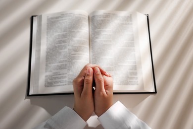 Photo of Above view of woman holding hands clasped while praying over Bible at white table