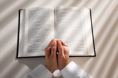 Above view of woman holding hands clasped while praying over Bible at white table