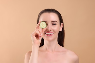 Photo of Beautiful woman covering eye with piece of cucumber on beige background