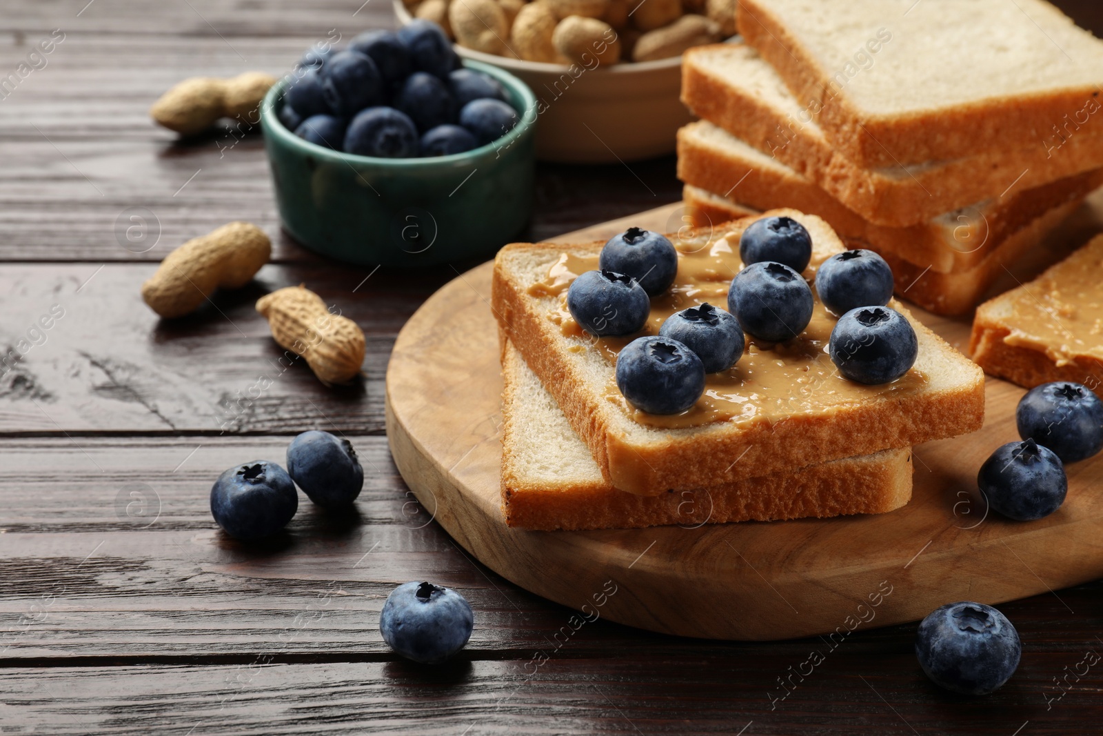 Photo of Delicious toasts with peanut butter, blueberries and nuts on wooden table, closeup. Space for text