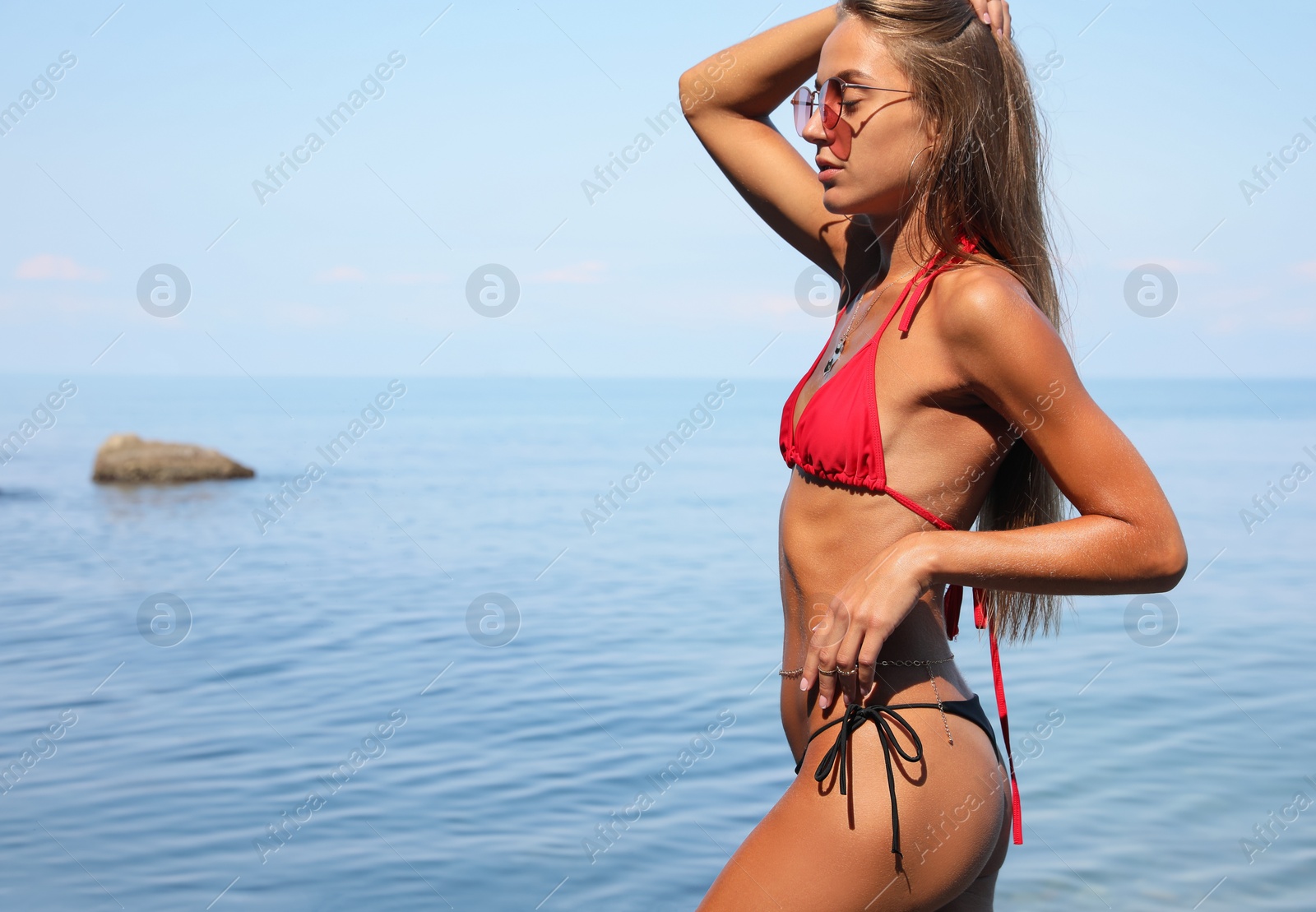 Photo of Beautiful young woman in stylish bikini and sunglasses on seashore, space for text