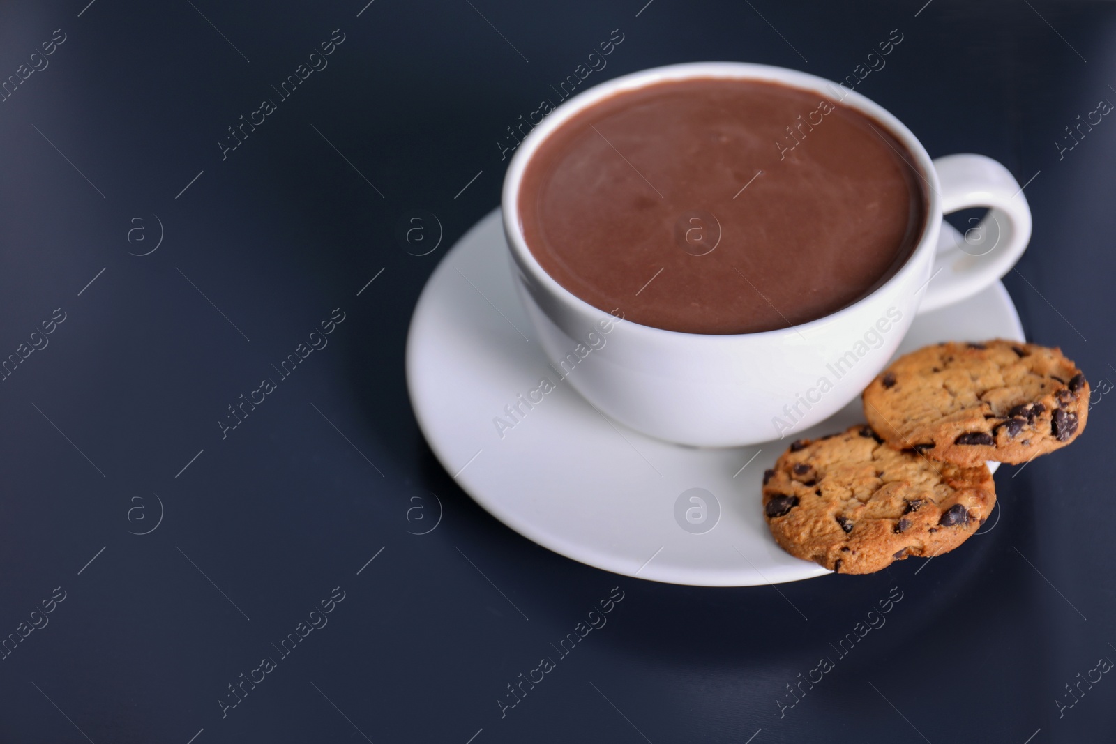 Photo of Cup of aromatic cacao with cookies on dark table. Space for text