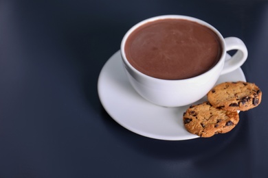 Photo of Cup of aromatic cacao with cookies on dark table. Space for text
