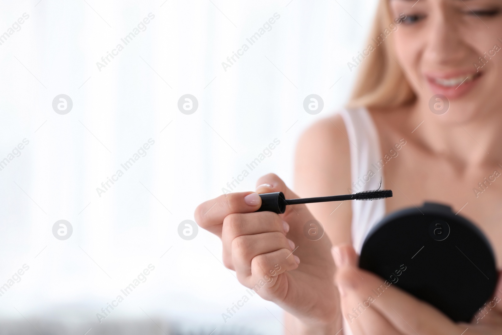 Photo of Emotional woman holding mascara brush with fallen eyelashes indoors