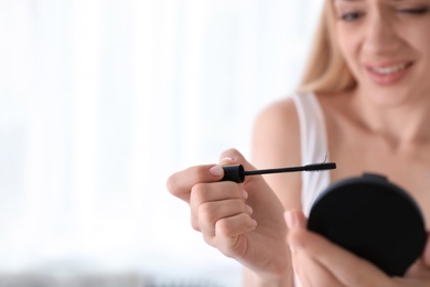 Photo of Emotional woman holding mascara brush with fallen eyelashes indoors