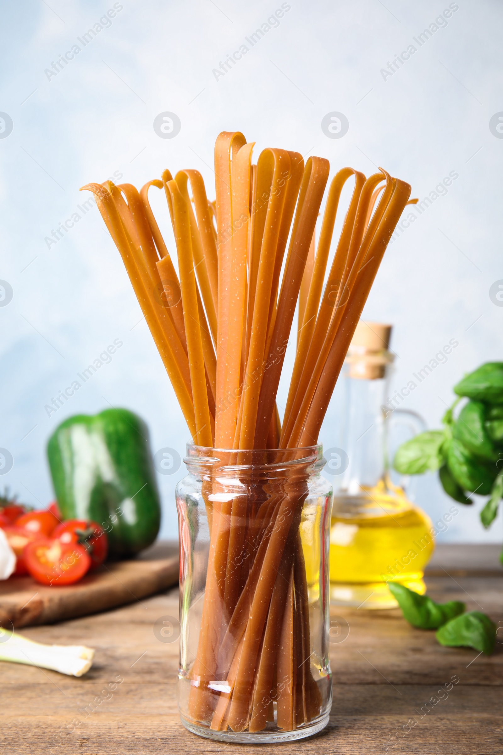 Photo of Jar with uncooked buckwheat noodles and fresh ingredients on wooden table