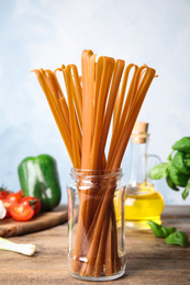 Jar with uncooked buckwheat noodles and fresh ingredients on wooden table