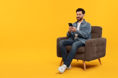 Photo of Happy man with smartphone sitting on armchair against yellow background. Space for text