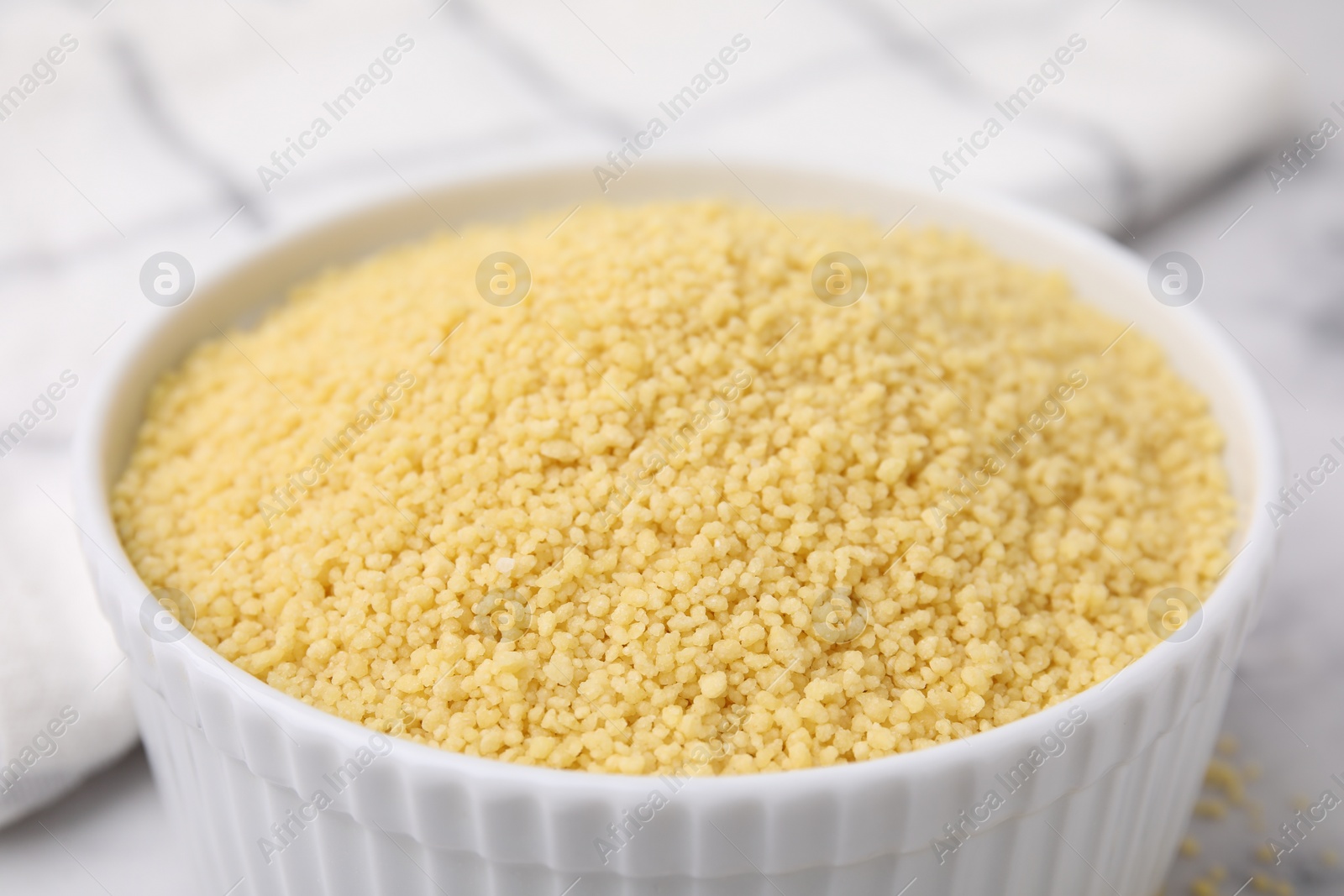 Photo of Raw couscous in bowl on light table, closeup