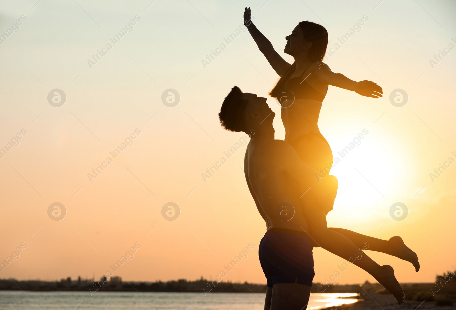 Photo of Young woman in bikini spending time with her boyfriend on beach at sunset. Lovely couple