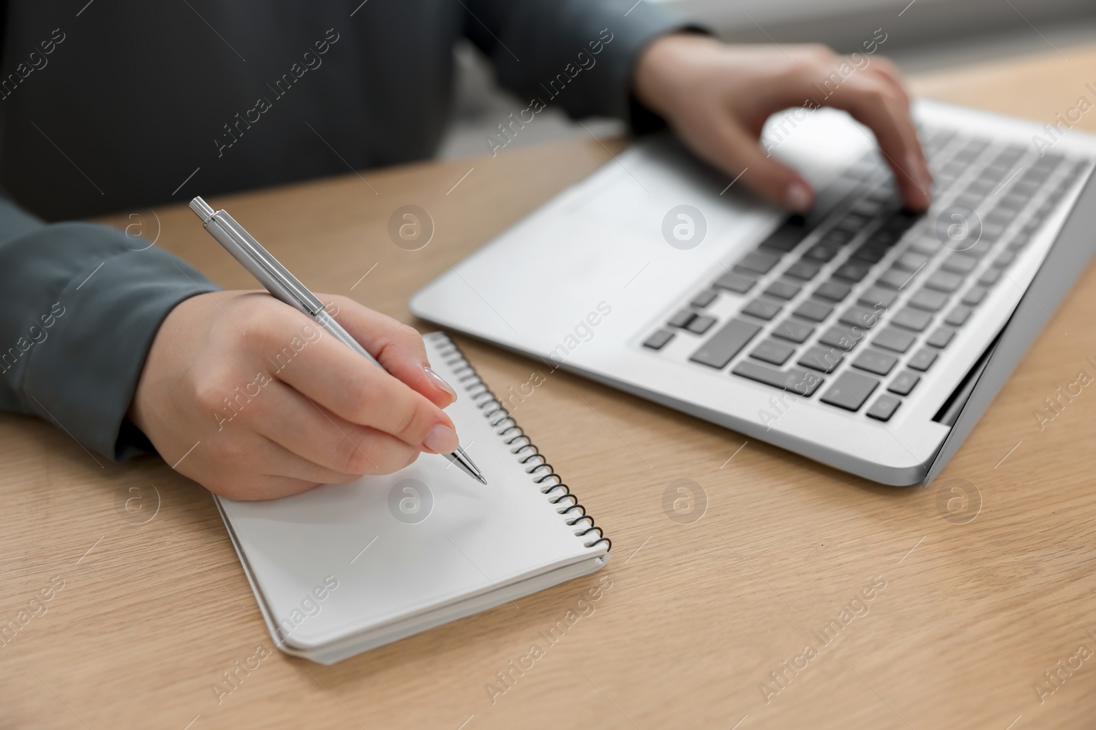 Photo of Woman with notebook and pen working on laptop at wooden table, closeup. Electronic document management