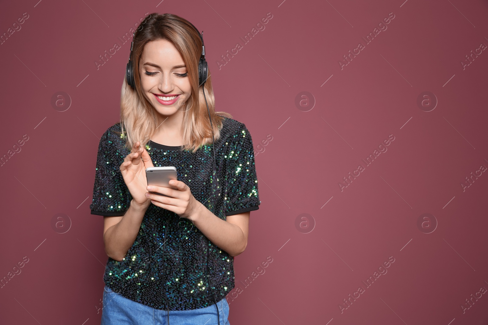 Photo of Young woman listening to music on mobile phone against color background