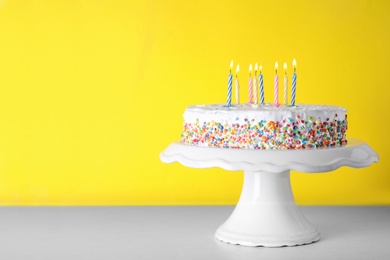 Photo of Birthday cake with burning candles on table against color background. Space for text