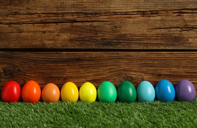 Photo of Bright Easter eggs on green grass against wooden background