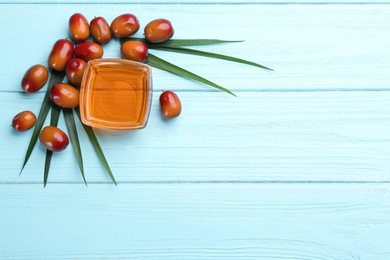 Photo of Palm oil in glass bowl, tropical leaf and fruits on light blue wooden table, flat lay. Space for text