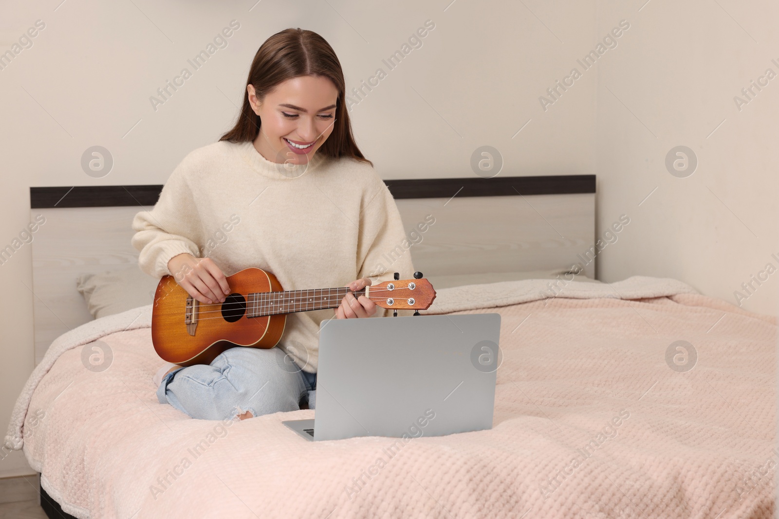 Photo of Happy young woman learning to play ukulele with online music course at home. Time for hobby