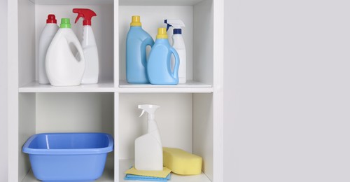 Photo of Shelving unit with different cleaning supplies and tools near white wall