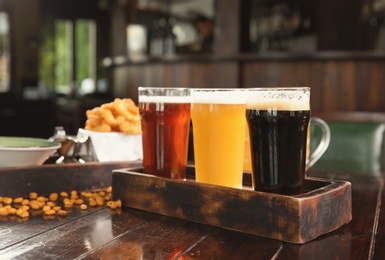 Glasses of tasty beer and snacks on wooden table in bar