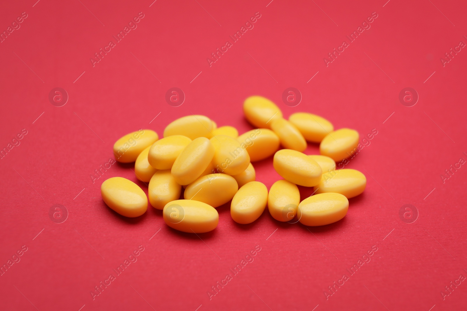 Photo of Many yellow dragee candies on red background