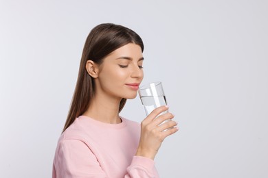 Photo of Healthy habit. Woman drinking fresh water from glass on light grey background