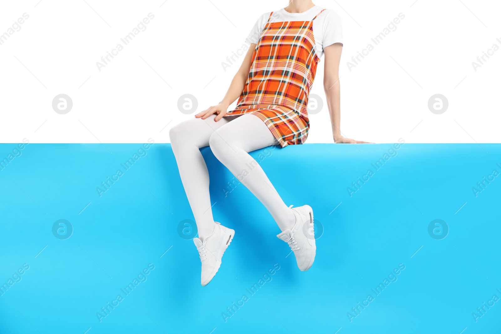 Photo of Woman wearing white tights and stylish shoes sitting on color background, closeup