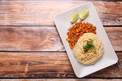 Photo of Tasty dish with fried minced meat, spaghetti, carrot and corn served on wooden table, top view. Space for text