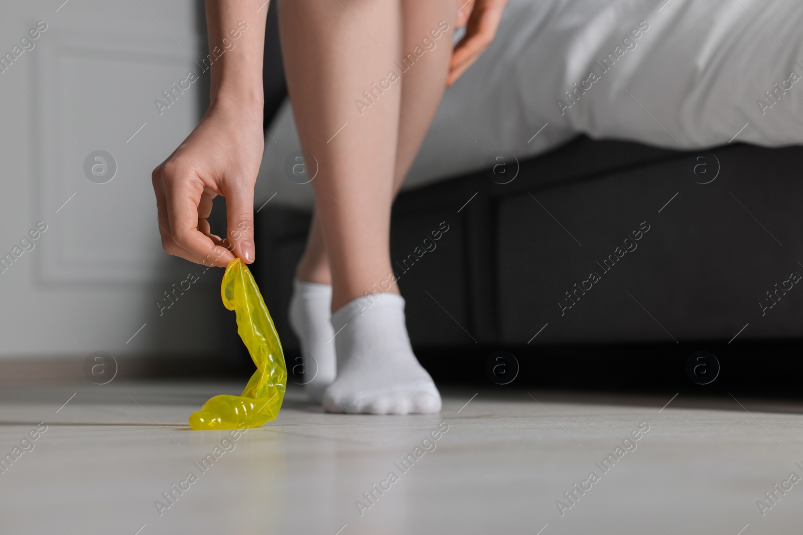 Photo of Woman taking unrolled condom from floor indoors, closeup. Safe sex