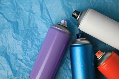 Cans of different graffiti spray paints on light blue crumpled paper, flat lay