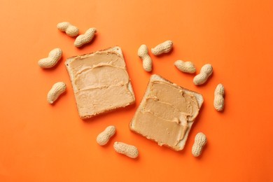 Photo of Tasty peanut butter sandwiches and peanuts on orange background, flat lay