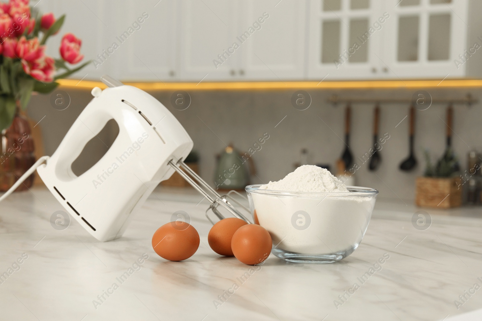 Photo of Modern mixer, eggs and bowl with flour on white marble table in kitchen