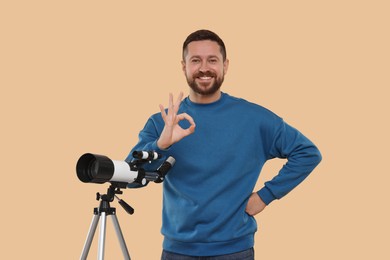 Photo of Smiling astronomer with telescope showing ok gesture on beige background