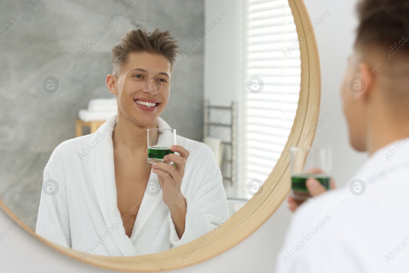 Photo of Young man using mouthwash near mirror in bathroom