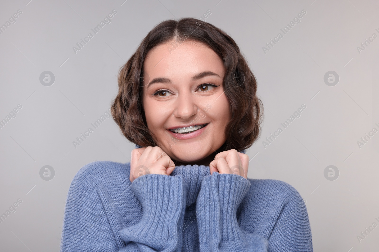Photo of Smiling woman with dental braces in warm sweater on grey background