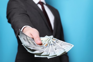 Man holding money on light blue background, closeup. Currency exchange