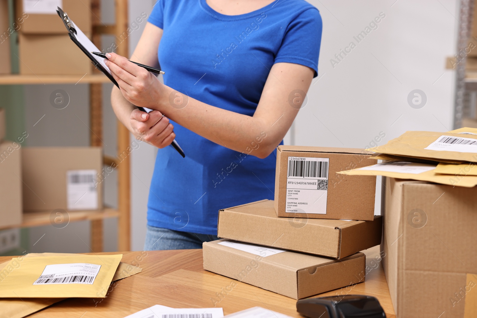 Photo of Parcel packing. Post office worker with clipboard at wooden table indoors, closeup