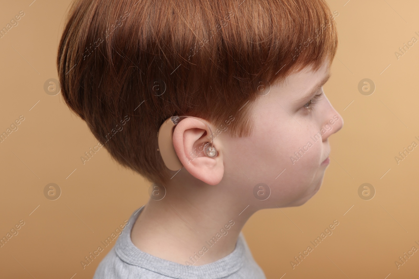 Photo of Little boy with hearing aid on pale brown background, closeup