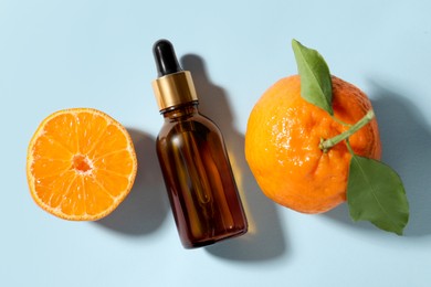 Aromatic tangerine essential oil in bottle and citrus fruits on light blue table, top view