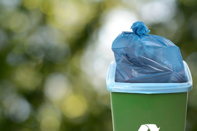 Image of Waste bin with plastic bag full of garbage on blurred background, space for text