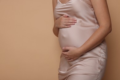 Photo of Pregnant woman in dress on beige background, closeup. Space for text