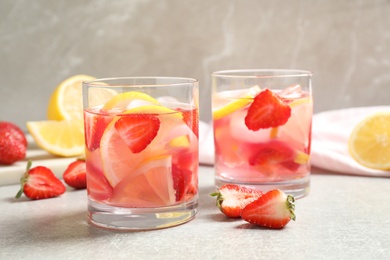 Tasty refreshing drink with strawberries and lemon on light grey table