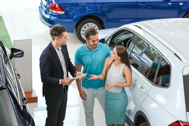 Photo of Salesman consulting young couple in car salon