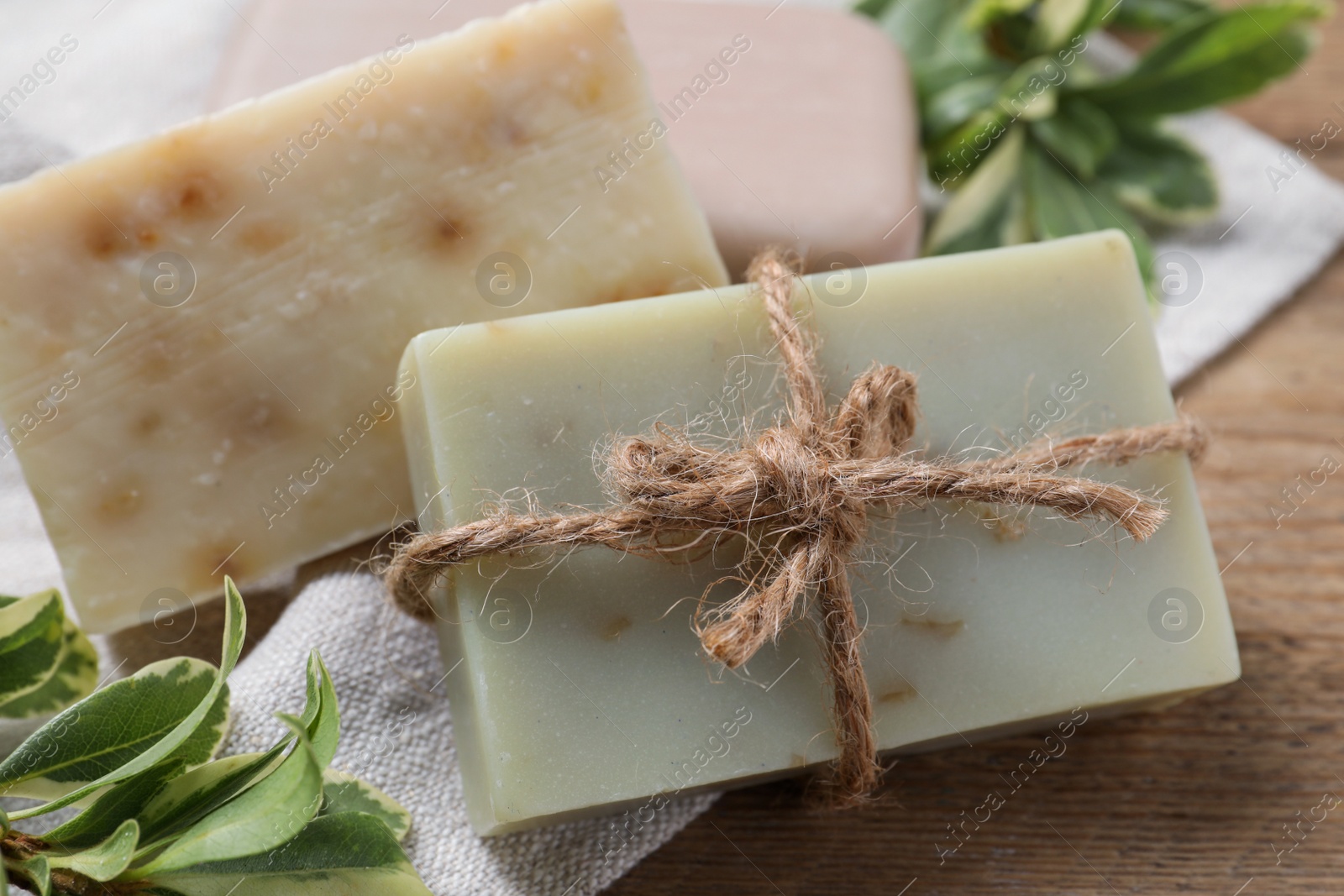Photo of Soap bars and green plants on wooden table, closeup