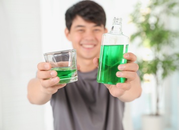 Man holding bottle and glass with mouthwash in bathroom. Teeth care