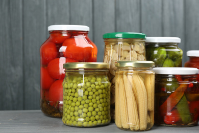 Glass jars with different pickled vegetables on grey wooden background