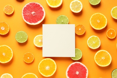 Fresh citrus fruits and blank card on color background, flat lay. Space for text