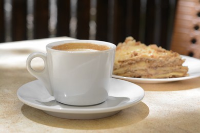 Photo of Cup of coffee and delicious cake on beige table, closeup